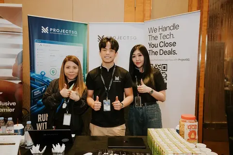 Three ProjectSG team members giving a thumbs up at an exhibition booth, in front of roll-up banners reading “We handle the tech. You close the deals.”