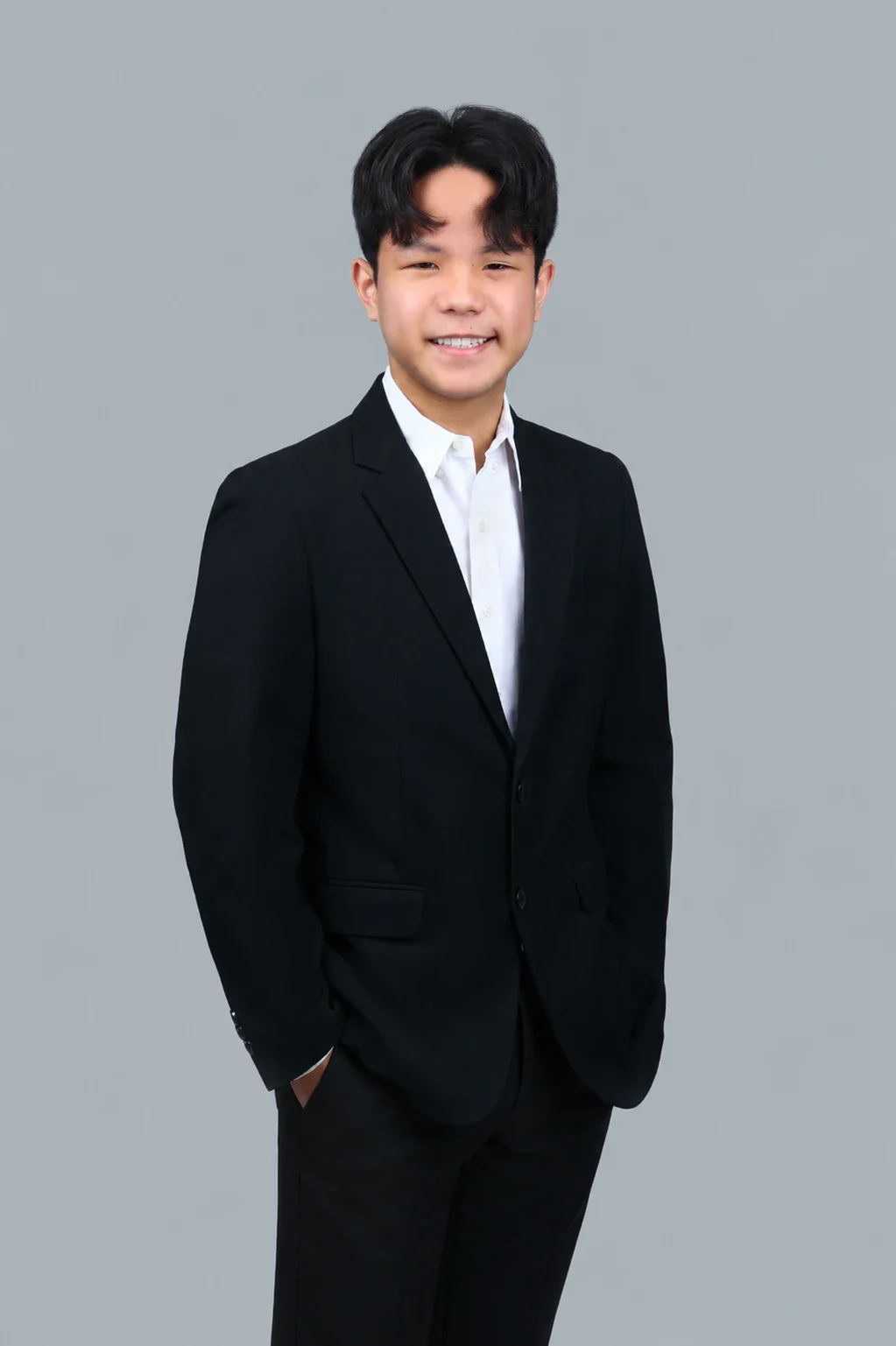 Asher Gan in a black suit and white shirt, standing with hands in pockets