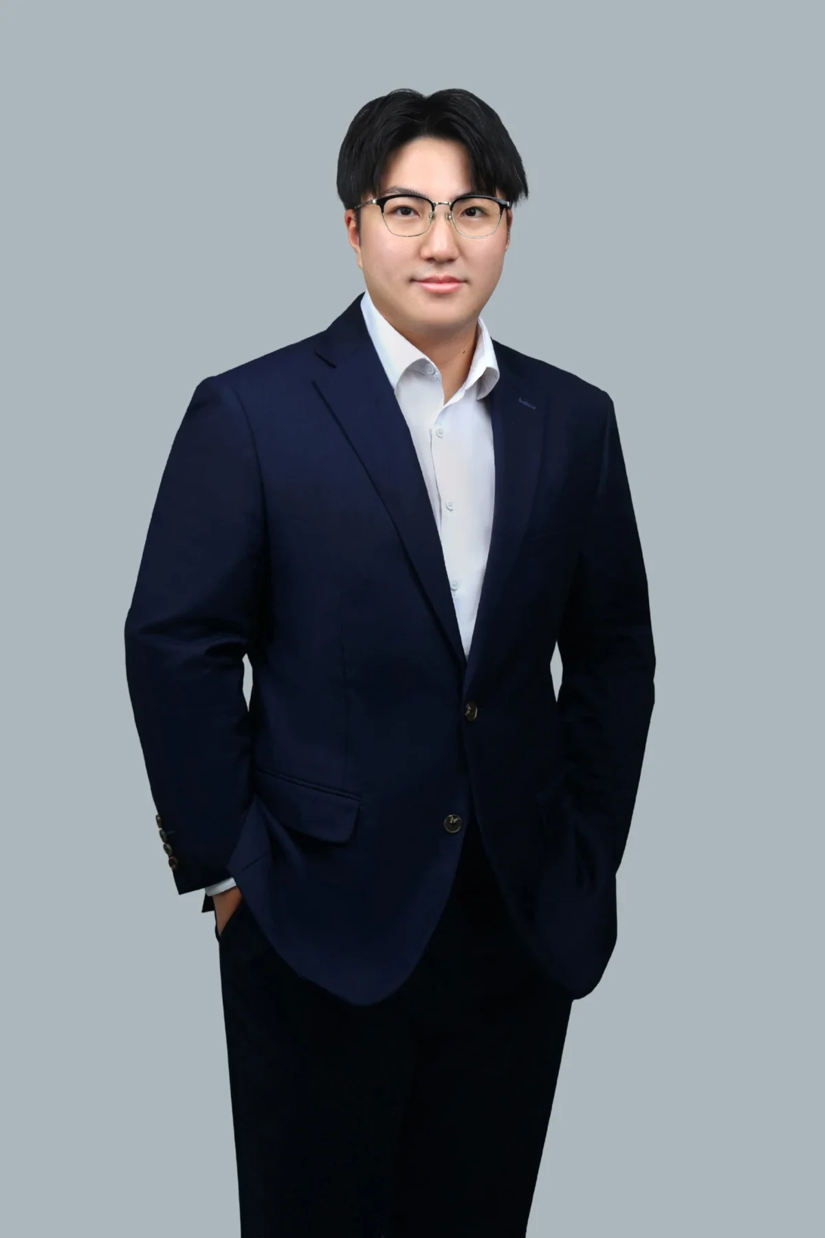 Jae Tan in a navy suit and white shirt, standing with hands in pockets